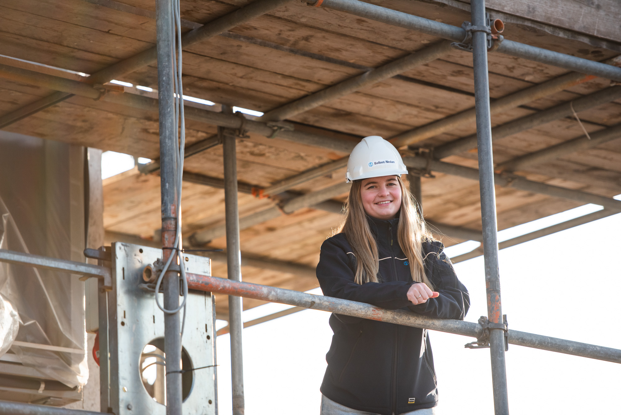 Danique van Vliet, werkvoorbereider bij Ballast Nedam West, gekleed in veiligheidskleding en een helm op een bouwplaats