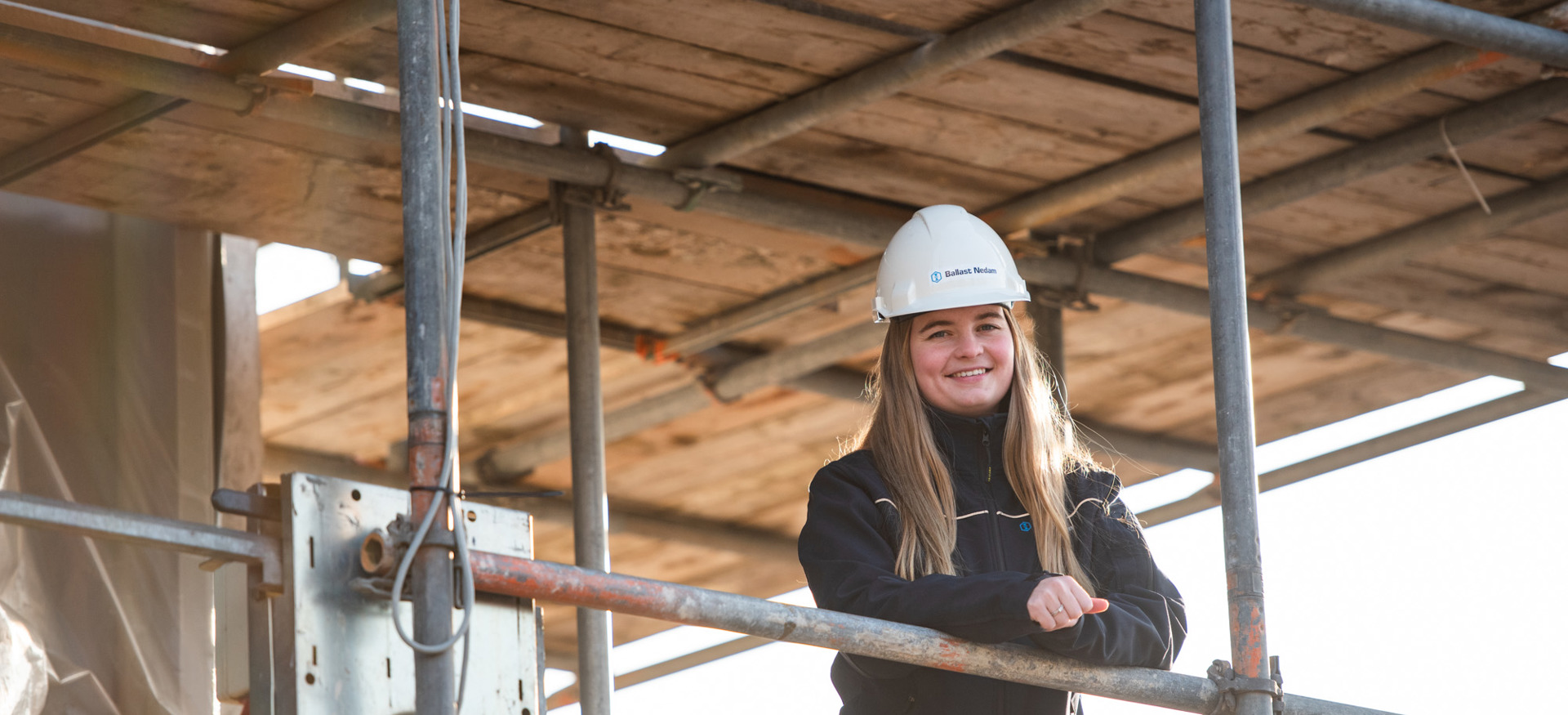 Danique van Vliet, werkvoorbereider bij Ballast Nedam West, gekleed in veiligheidskleding en een helm op een bouwplaats